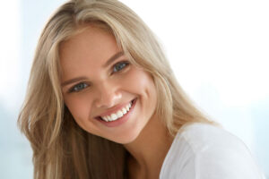 Young woman with implanted teeth on color background, closeup